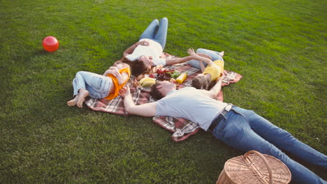 familia feliz tirada en una manta en el parque, riendo y divirtiéndose juntos mientras hacen un picnic en el parque