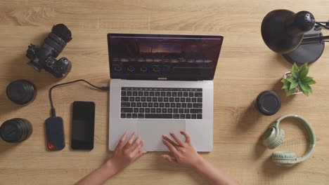 top view close up of woman color grading's hands using a laptop next to the camera editing the video in the workspace at home