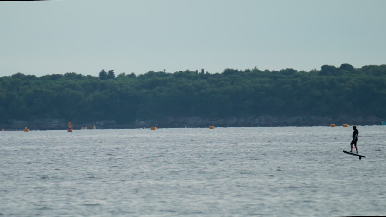 A man balances on an electric foilboard gliding smoothly over the water near the coast
