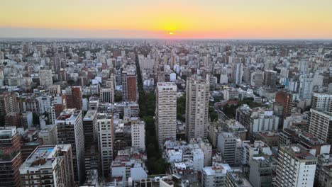 dolly out flying over belgrano neighborhood buildings at sunset with bright sun in horizon, buenos aires, argentina