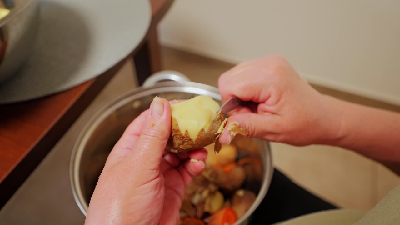 Close up of elderly hands peeling potato skin slowly in overhead rustic kitchen