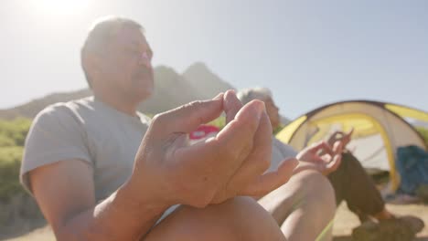 Happy-senior-biracial-couple-at-tent-in-mountains-meditating-on-sunny-day,-in-slow-motion