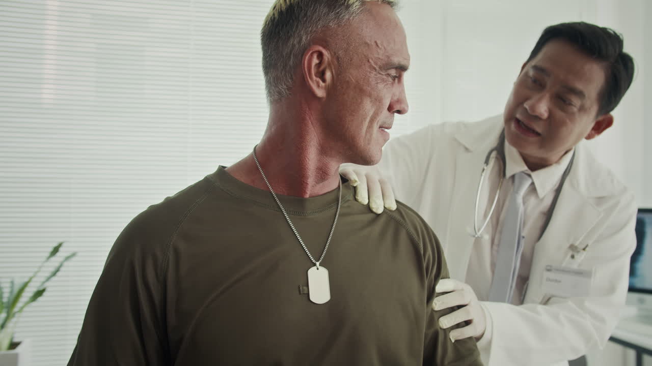 Asian Doctor Asking Middle-aged Serviceman about Injured Arms at Clinic