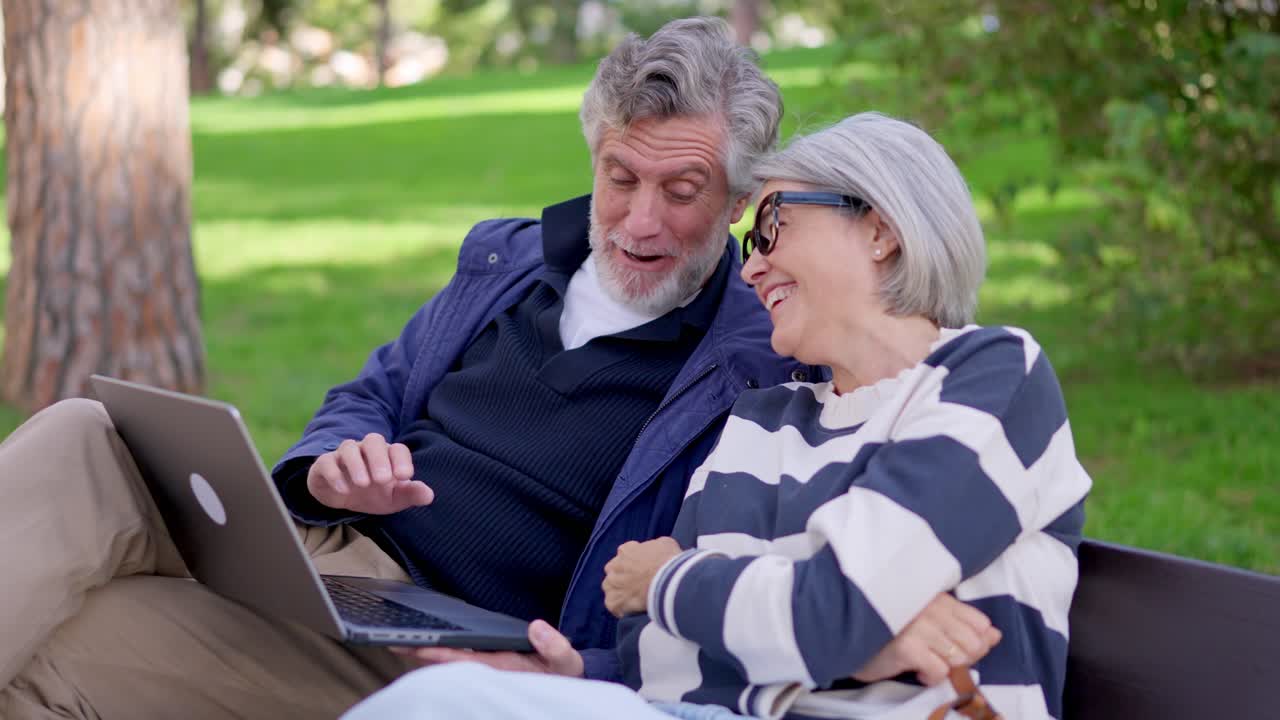 Una felice coppia di anziani ride mentre usa un laptop nel parco