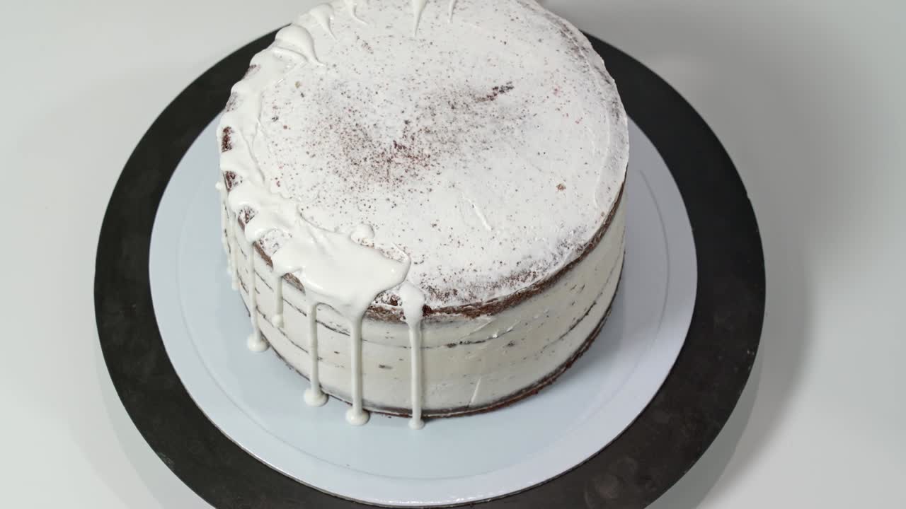 Vista dall'alto di un pasticcere che versa cioccolato bianco fuso sui bordi della torta in modo che coli lungo i lati.
