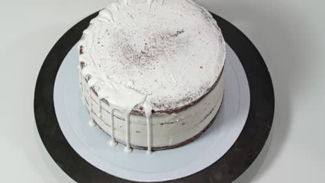 top view of a baker pouring melted white chocolate on the edges of the cake so it drips down the sides.