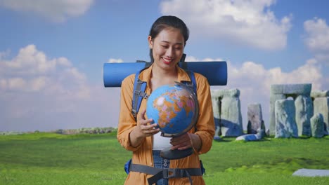 asian female hiker with mountaineering backpack holding world globe in her hands and smiling while traveling in stonehenge