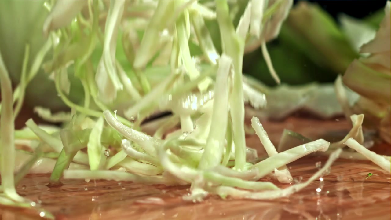 Shredded Cabbage Falling on Wet Wooden Board in Slow Motion