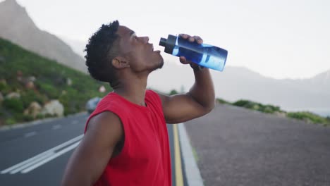 hombre afroamericano bebiendo agua mientras está de pie en la carretera