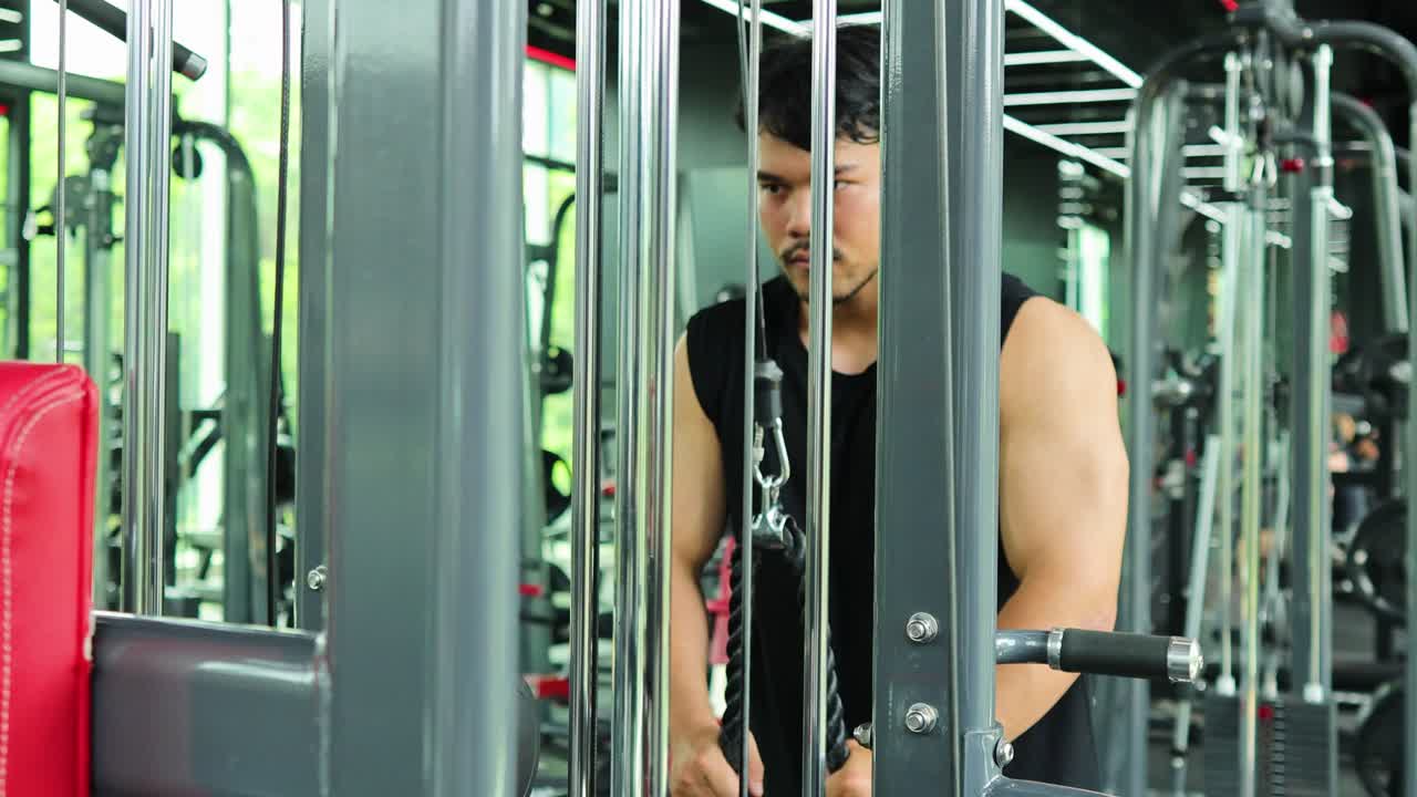 A focused individual performs a cable machine exercise in a well-lit, modern gym setting, emphasizing strength and determination