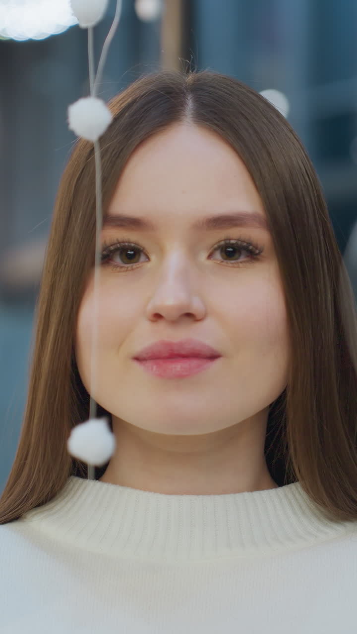 Young woman in white sweater gently interacts with a hanging white ornament in a mall, showcasing a playful and warm pose against a backdrop of festive decorations