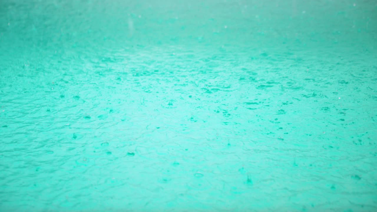 Medium wide shot of several rain drops hitting pool surface and creating turbulence on the water surface in slow motion
