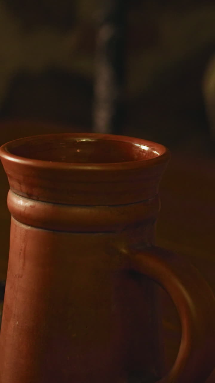 el criado medieval pone la taza de cerveza en el mostrador de madera de primer plano. el barman sirve bebidas alcohólicas en platos de arcilla en la taberna. bebiendo vino en un pub anticuado
