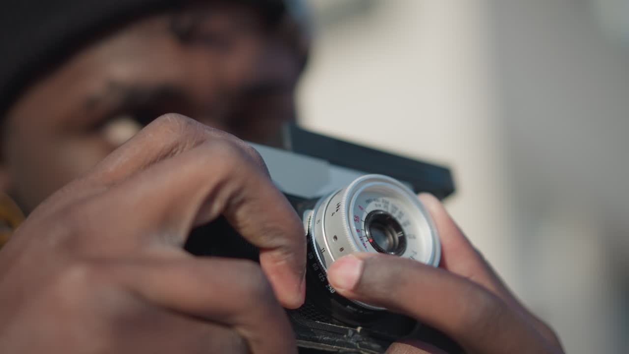 close up of hands of photo enthusiast handling vintage camera, fingers delicately turning focus ring to adjust lens under soft sunlight, snowy urban background creating cinematic vibe