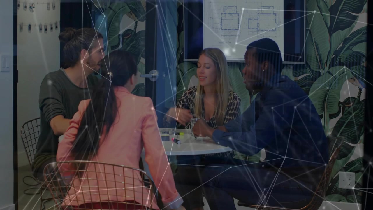Office team sitting at table, passing markers and sparking brainstorming, network overlaying scene
