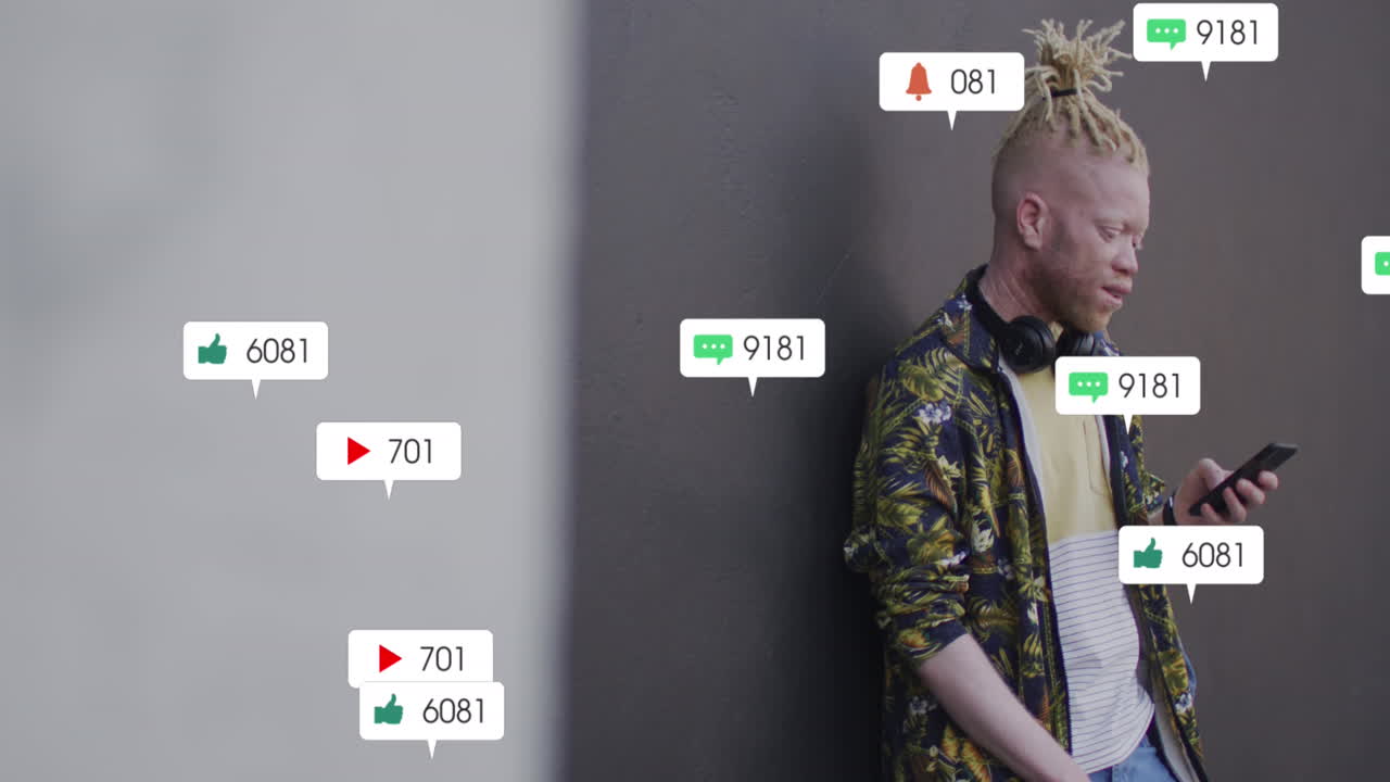 animación de iconos de redes sociales sobre un hombre albino usando un teléfono inteligente de pie contra una pared gris