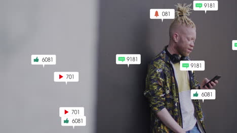 animation of social media icons over albino man using smartphone standing against grey wall