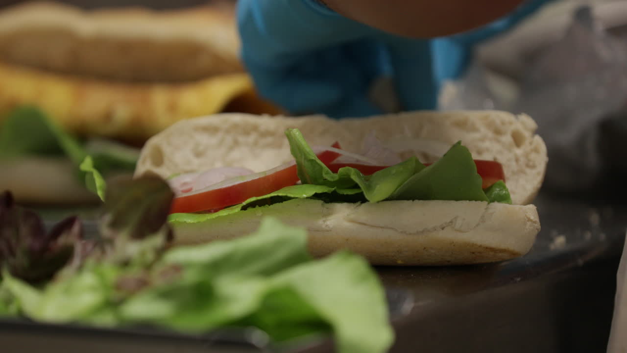 Persoon in handschoenen bereidt en maakt een tonijnsandwich met verse groenten.