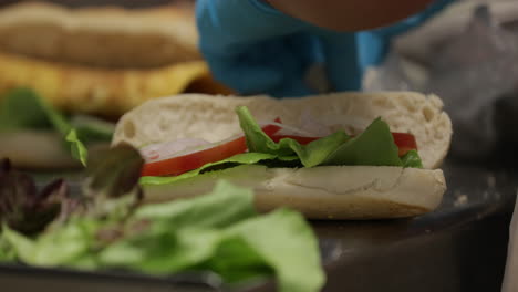 persona con guantes preparando y preparando sándwich de atún con verduras frescas.