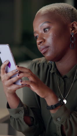 a young black woman with short hair looks at her phone while smiling.