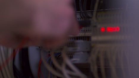 A-focused-technician,-with-a-blurred-face,-diligently-working-on-an-active-server-rack,-bathed-in-the-glow-of-three-red-lights,-in-a-room-filled-with-machinery-and-equipment,-caught-by-a-static-camera