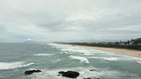 Port-Macquarie,-Australia---The-Sensational-Scenery-Of-The-Waves-Splashing-into-the-Shore-With-Green-Trees-and-Cloudy-Sky-Above---Wide-Shot