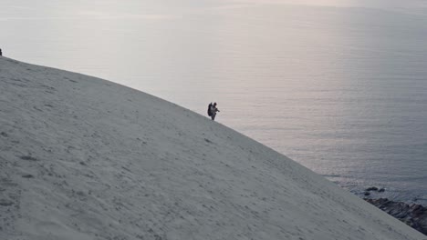 person standing on sandy hill looking at beautiful sea and beach at sunset in norway