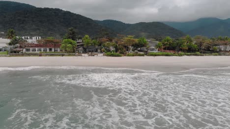 Drone-footage-of-the-beach-above-the-sea,-mountain-in-front-of-the-sea,-cloudy-day,-waves,-landscape-of-Juquehy,-Ubatuba,-northern-coast-of-São-Paulo,-Brazil