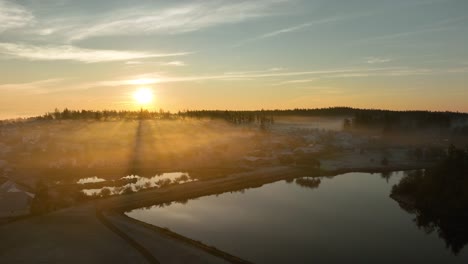 Rising-aerial-view-of-a-pond-surrounded-by-the-morning-fog-and-warm-sunrise