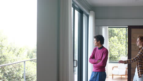 feliz pareja gay diversa mirando por la ventana y abrazándose en casa, cámara lenta, espacio de copia