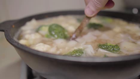 chopped vegetables cooking in broth being stirred with wooden spoon authentic rustic chef home