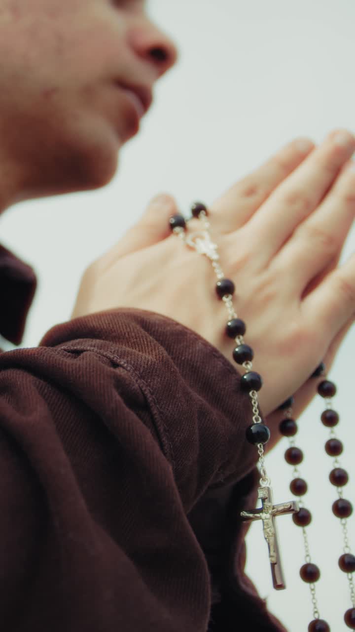 Mani di un uomo religioso che prega con un rosario e un crocifisso