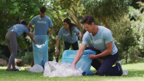 Un-Hombre-Caucásico-Sonriente-Y-Un-Grupo-Diverso-De-Amigos-Poniendo-Basura-En-Sacos-De-Basura-Azules-En-El-Parque