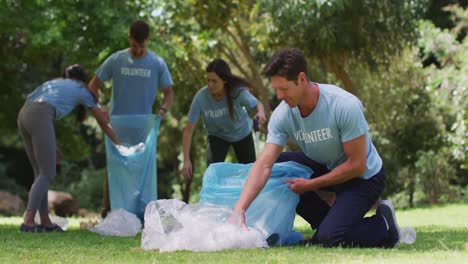 hombre caucásico sonriente y un grupo diverso de amigos poniendo basura en bolsas de basura azules en el parque