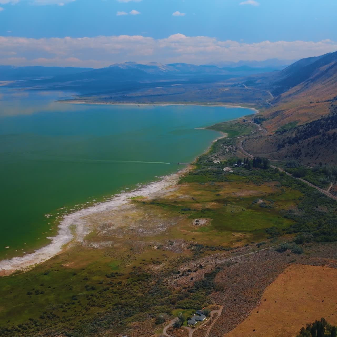 Azure skies reflecting in the beautiful calm waters of the lake. Bare mountains towering over the Mono Lake at backdrop of sky with white clouds