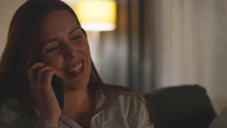 Close-Up-Of-Smiling-Woman-Sitting-On-Sofa-At-Home-At-Night-Talking-On-Mobile-Phone-Shot-In-Real-Time-1