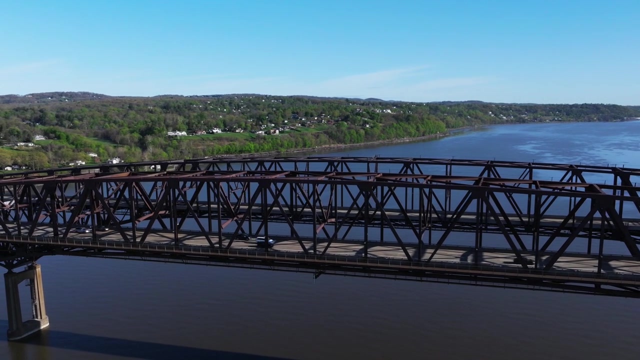 Newburgh-Beacon Bridge truss spans the Hudson River against wooded New York hills, aerial orbit establishing