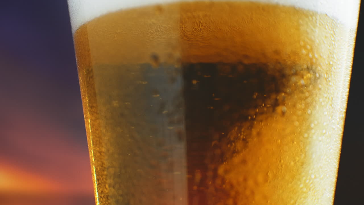la cerveza fría macro en cámara lenta se vierte en un vaso con transpiración. las burbujas de cerveza suben a la superficie.
