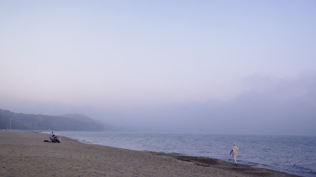 A person walking on an empty foggy beach during sunrise