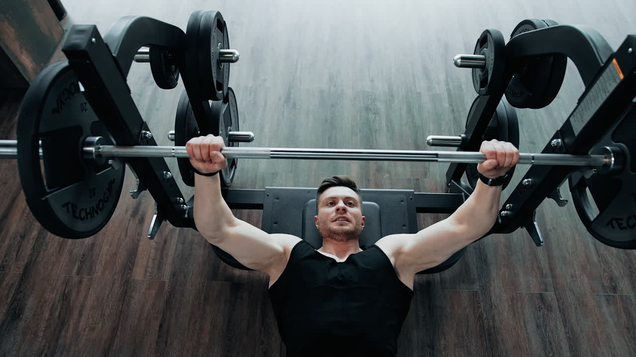 Muscle Man Lifting Weight At Gym. Young athlete doing bench press in gym