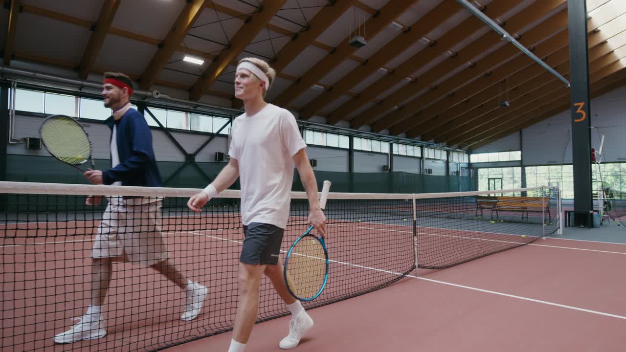 двое мужчин пожимают руки на крытом теннисном корте.