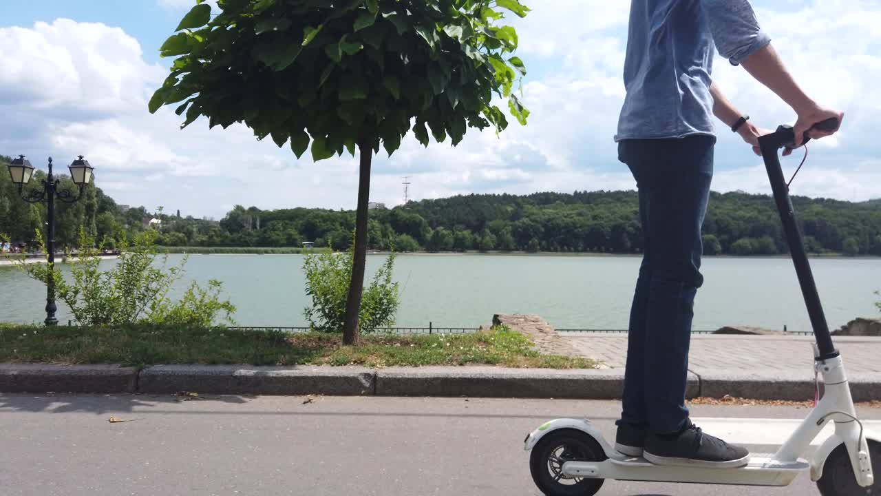 CHISINAU, MOLDAVIA - 9 DE JULIO DE 2019: Hombre montado en un patinete eléctrico blanco en el parque Valea Morilor. Lago al fondo