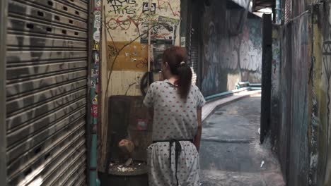 Movimiento----Mujer-Tailandesa-Asiática-Solitaria-Fumando-Un-Cigarrillo-Mirando-Pinturas-En-La-Pared-En-Un-Callejón-Estrecho-En-Bangkok,-Tailandia----Tiro-De-Cardán-Estabilizado-Mujer-Que-Pasa----Tiro-Gran-Angular-Full-Hd