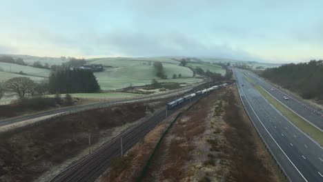freight train disappearing under m6 motorway bridge at dawn in winter amongst rural setting