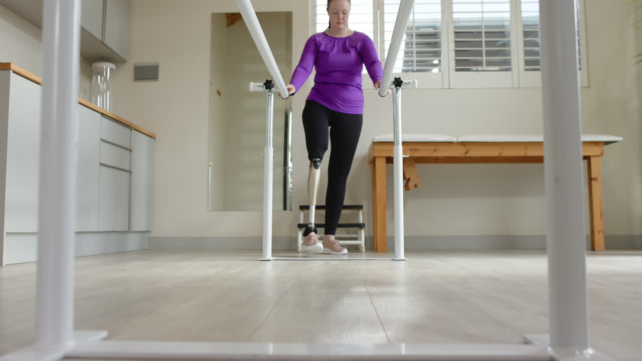A woman with prosthetic leg walking between parallel bars in a rehab room