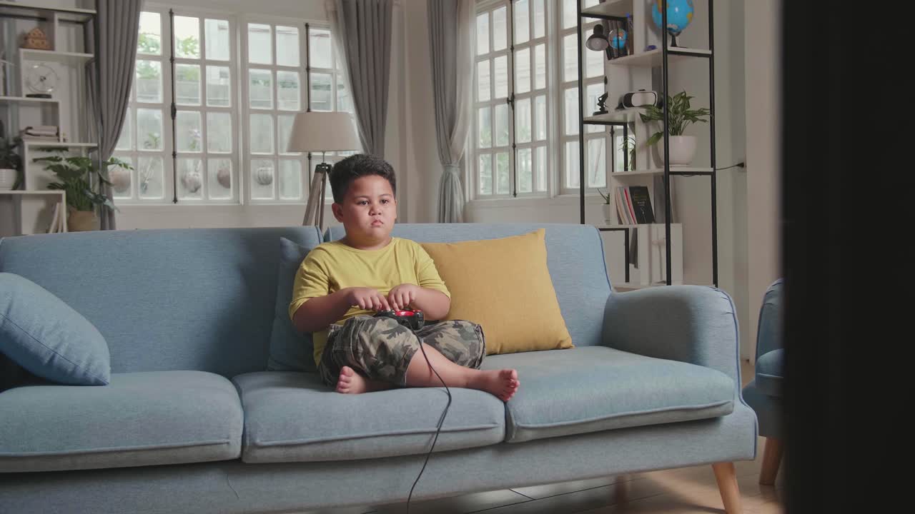 Young Boy Using His Fingers Playing Game At Home, Sitting On A Couch