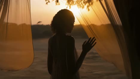 silhouette of a young woman gently touching soft, transparent curtains while basking in the warm glow of a golden sunset, embracing the tranquility of a serene landscape