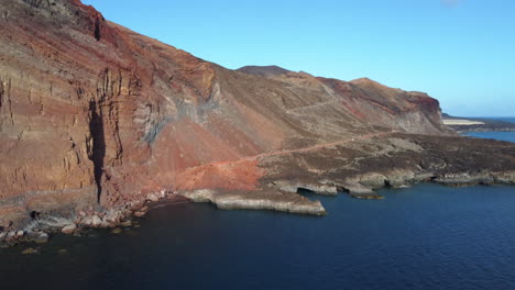 acercándose a las altas rocas rojas ocre iluminadas por el sol, la isla después de la actividad volcánica rodeada de mar claro y tranquilo, cala tacoron, el hierro