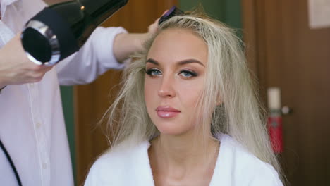 blonde woman sits on chair stylist does hairstyle in salon