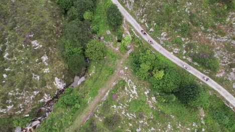 Several-people-on-horseback-move-along-the-gray-road-between-the-green-nature-in-Valles-Pasiegos-in-Spain